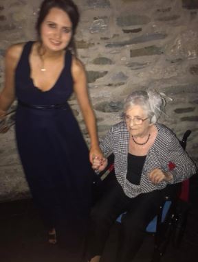 Catherine in 2017 in a navy blue dress, holding the hand of her wheelchair-bound Grandmother.